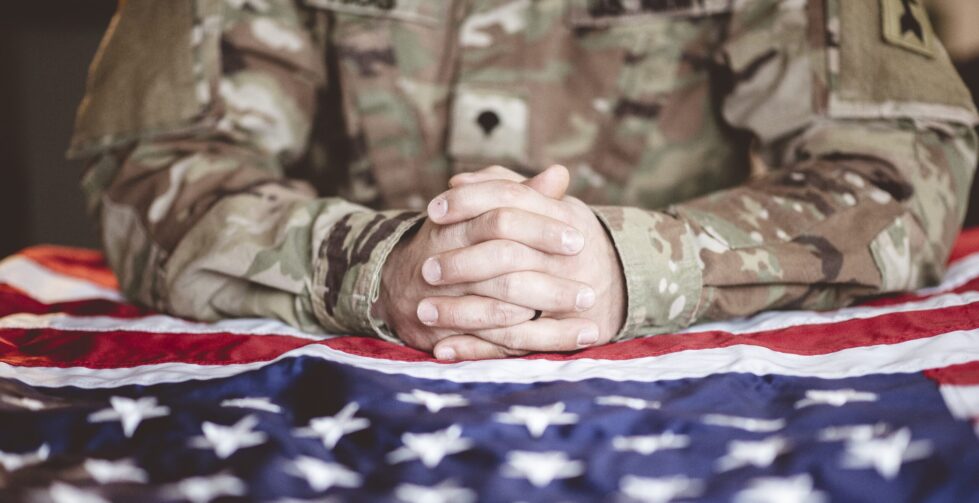 Newark Council approves Veterans Memorial Chair 1 american soldier mourning praying with american flag front him scaled e1747848375578